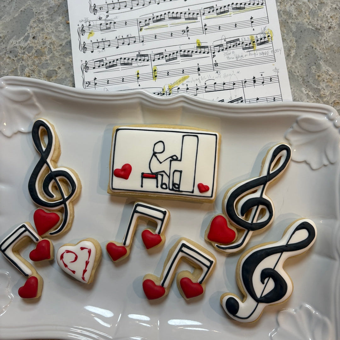 Decorative cookies shaped like musical notes and hearts on a white plate with sheet music in the background.