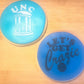 Two blue coasters with 'UNC' and 'Let's Get Crazie' text on a wooden surface