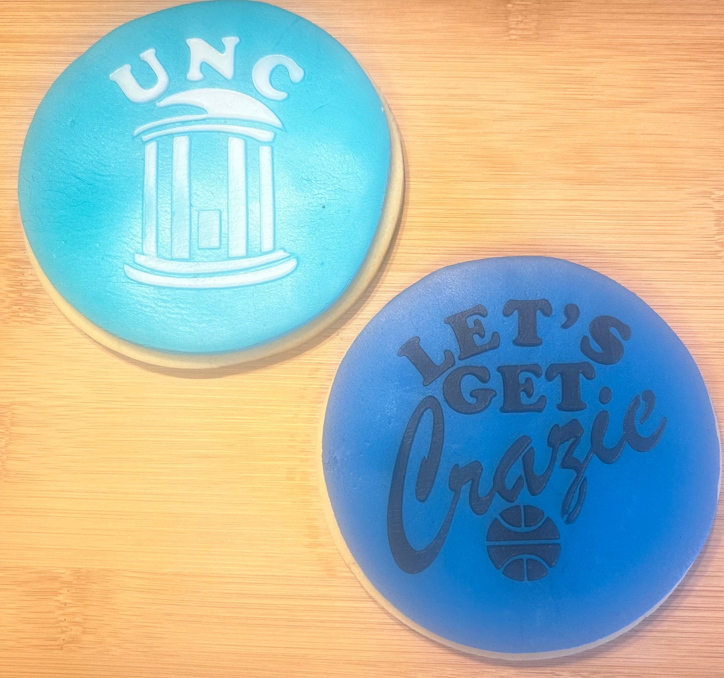 Two blue coasters with 'UNC' and 'Let's Get Crazie' text on a wooden surface