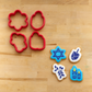Cookies flooded with royal icing and stenciled with the Hanukkah Trinkets Cookie Stencils lying next to their matching cookie cutters.