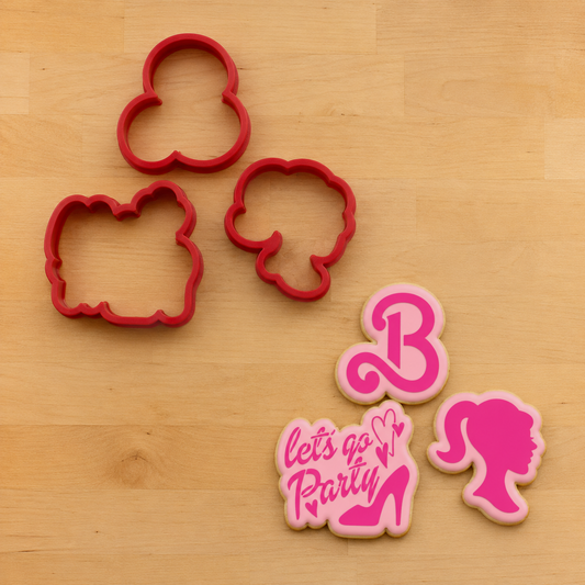 Three red cookie cutters arranged on a light wood surface, alongside three pink decorated sugar cookies featuring a Barbie and a high-heel silhouette with the words "let's go Party" and a heart.