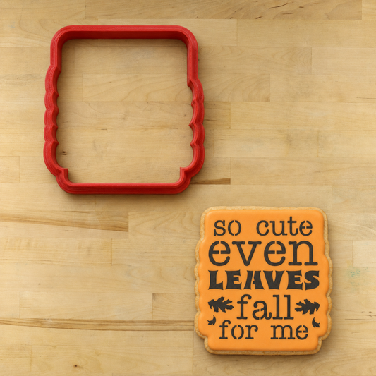 Cookie iced in orange, and decorated with the "Leaves Fall For Me" cookie stencil, lying next to the matching cookie cutter.