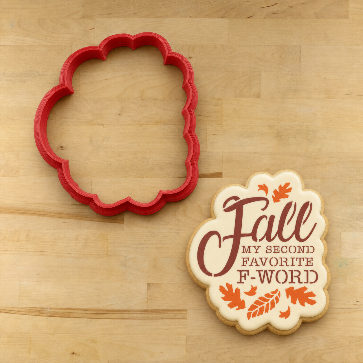 Funny Fall Cookie iced and stenciled with a "Fall is my second favorite f-word" cookie stencil, lying next to the matching cookie cutter