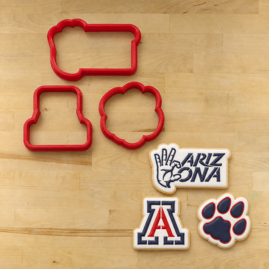 Three red cookie cutters and three decorated Arizona Wildcats-themed cookies arranged on a light wood background.