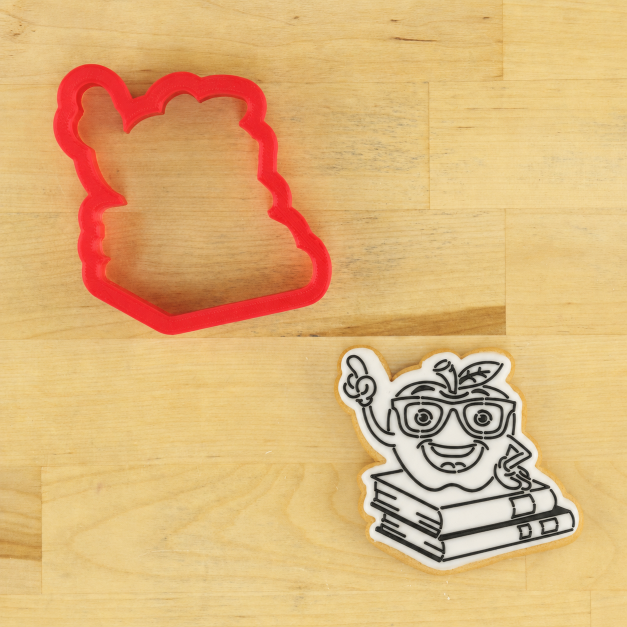 One Smart Apple Cookie stencil, applied to a white, iced cookie lying next to the matching cookie cutter.