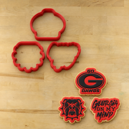 Three red cookie cutters and three decorated sugar cookies featuring the Georgia Bulldogs logo and the phrase 'GEORGIA ON MY MIND' on a light wood background.