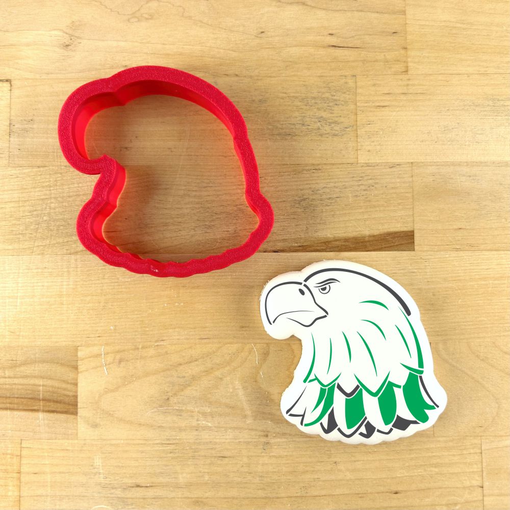 Eagle head mascot cookie stencil and red cutter on wooden surface for sports-themed baking.