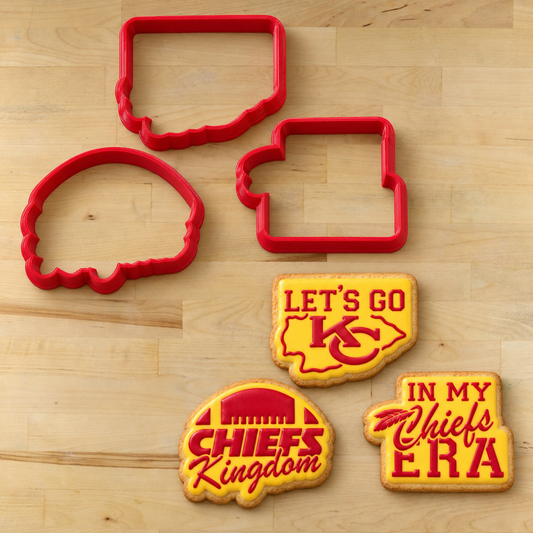 Four red cookie cutters arranged on a light wood surface, with four decorated cookies shown below them featuring Kansas City Chiefs-themed designs: a Chiefs logo cookie reading 'LET'S GO', a football cookie reading 'CHIEFS Kingdom', and a script cookie reading 'IN MY Chiefs ERA'.