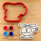Helicopter Paint Your Own Cookie lying next to a matching helicopter shaped cookie cutter, artist brush and food coloring