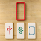 Three white rectangular cookies with Chinese mahjong-style symbols and a red rectangular cookie cutter, arranged on a light wood surface.