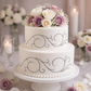 Scrollwork Cake Stencil pattern applied to the sides of a 2-tiered wedding cake topped with purple roses.