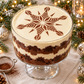 Layered chocolate trifle in a glass pedestal bowl with a cocoa crystal snowflake dusted onto its pale cream topping.