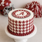 Cake with Alabama Crimson Tide design on a white stand, surrounded by football helmet and pom-pom.