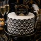 Black and white patterned birthday cake with 'Happy Birthday' topper, surrounded by champagne glasses and decorative feathers.