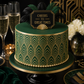 Green and gold cake with 'Cheers to Great Times' topper, surrounded by champagne glasses and decorative elements.