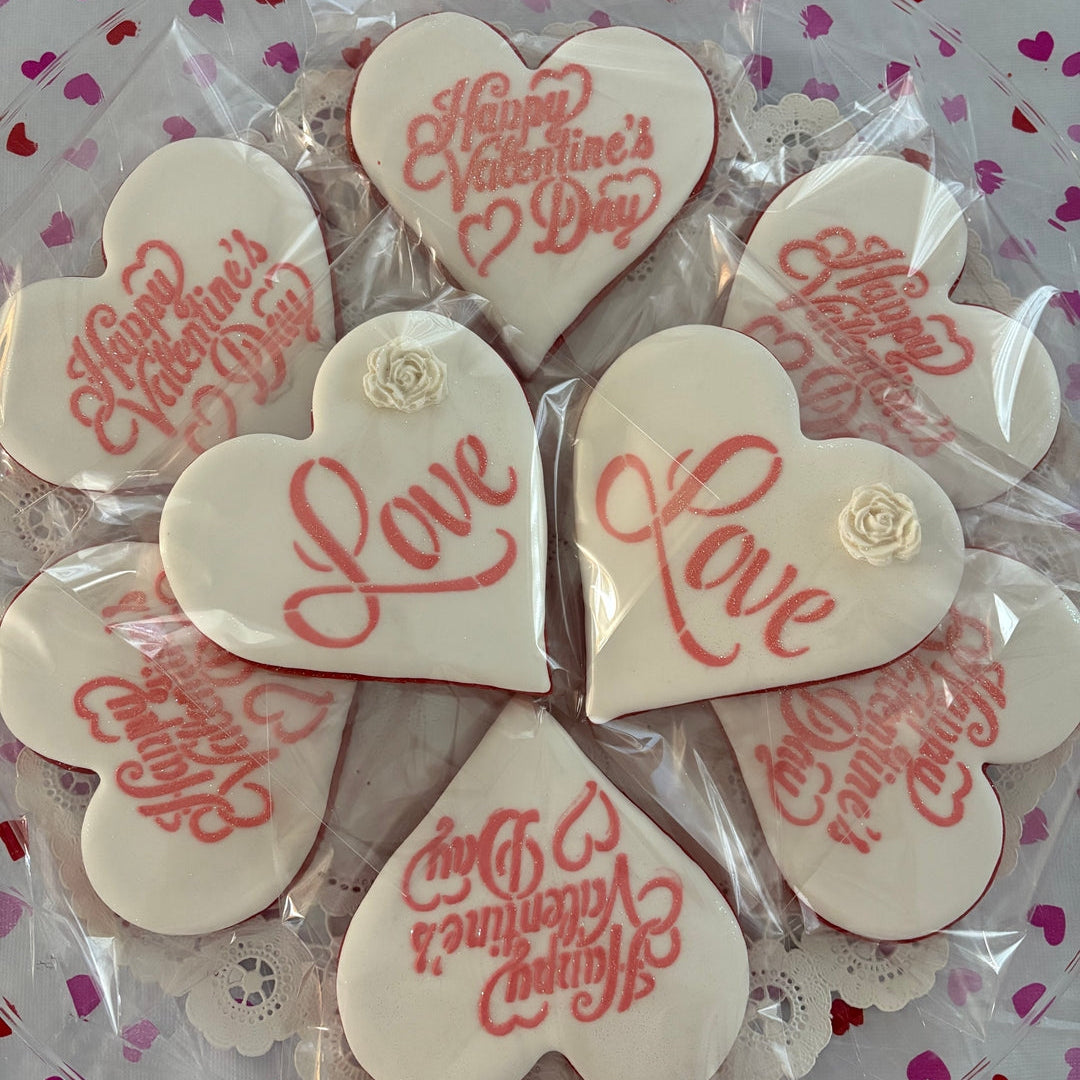 Heart-shaped cookies with 'Happy Valentine's Day' and 'Love' text on a pink heart-patterned background.