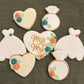 Decorative cookies shaped like a heart, ring, and dress on a textured surface.
