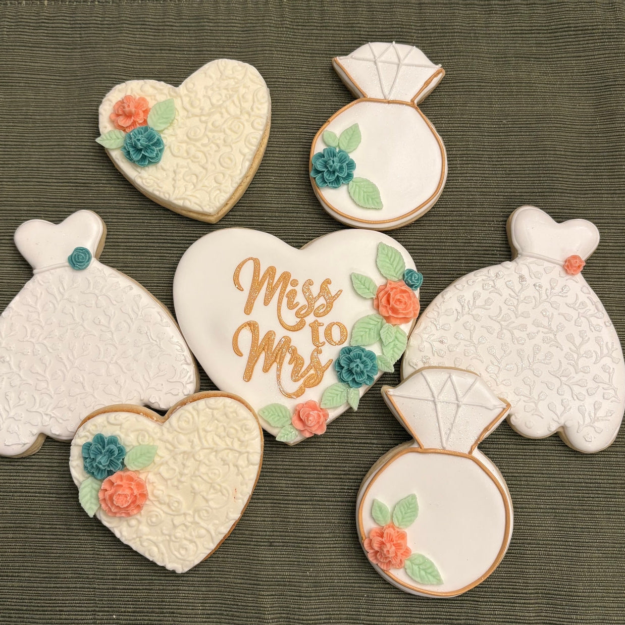 Decorative cookies shaped like a heart, ring, and dress on a textured surface.