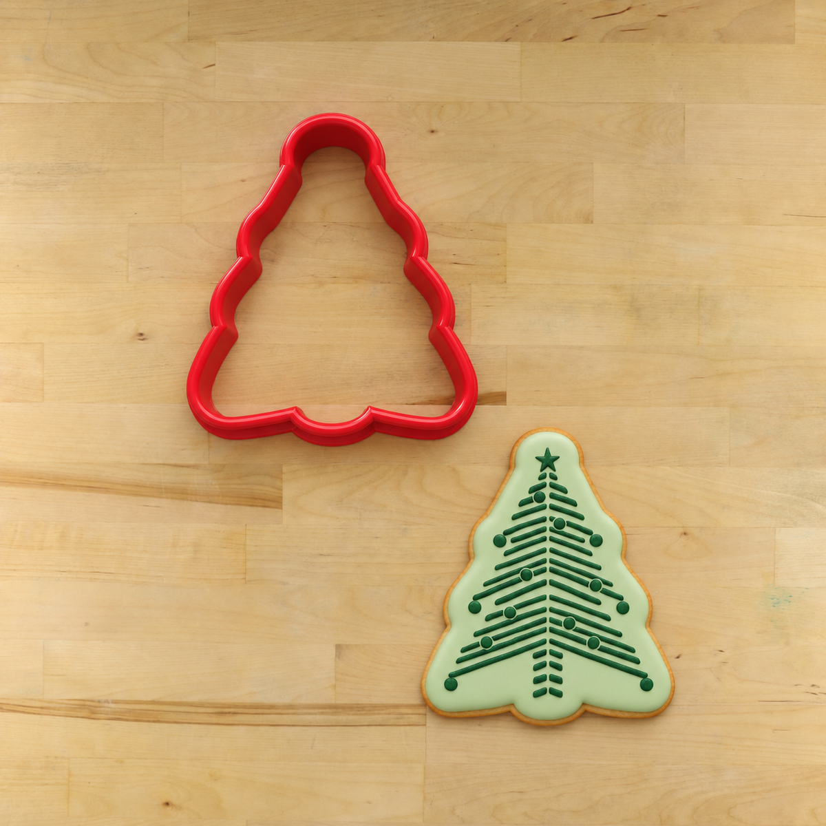 A flooded cookie that has been stenciled with the Chevron Christmas Tree Cookie Stencil and is lying next to its matching cookie cutter.